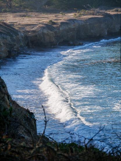 A wave washing toward a shore, with the sunlight illuminating the sea foam