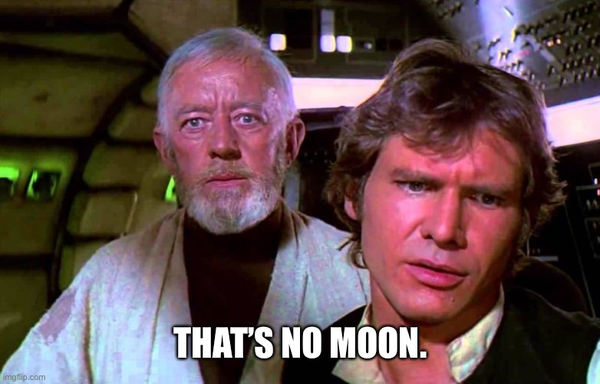 Screenshot from the Star Wars movie inside the cockpit of the Millennium Falcon with Obi-Wan Kenobi in mid-shot looking forward with apprehension and Han Solo in the foreground right looking down with confusion. The caption reads 'That's no moon'