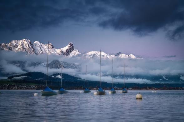 Thunersee am Morgen mit schneebedeckter Bergkette im Hintergrund und Segelbooten an Bojen.