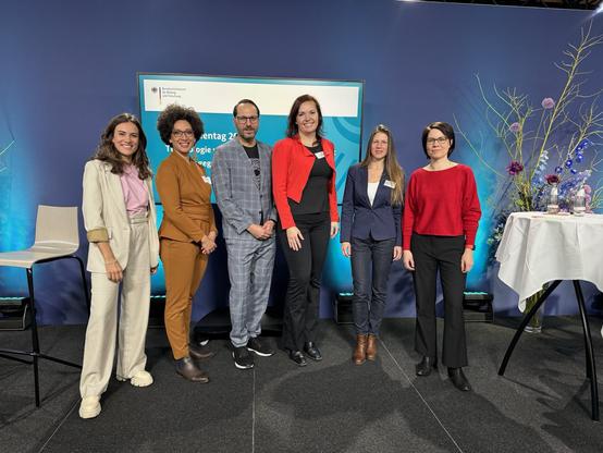 Gruppenbild der Panelteilnehmenden zusammen mit der Moderatorin auf der Bühne