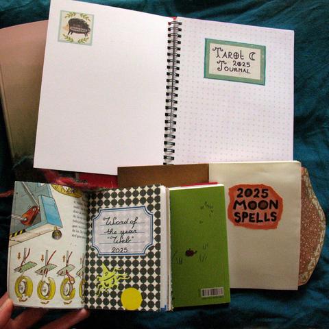 Pile of journals of different sizes laying open on their title pages. One with a label that says "tarot journal 2025", another has written "moon spells 2025" and another a label with "word of the year: web, 2025".