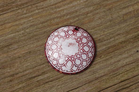 Un médaillon rond en cuivre gravé puis émaillé en blanc, posé sur du bois.