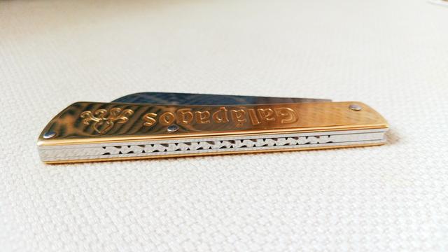 Un couteau de poche avec un manche en laiton, vu du dessus. Le ressort est guilloché.