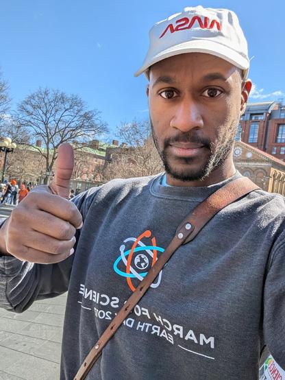 Me giving a thumbs up wearing a NASA cap and my old March for Science sweatshirt