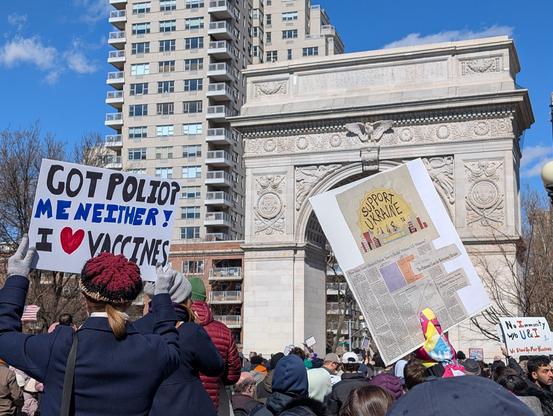 A scientist holding a sign that says "Got Polio? Me Neither! I ❤️ Vaccines

Another sign that says Support Ukraine