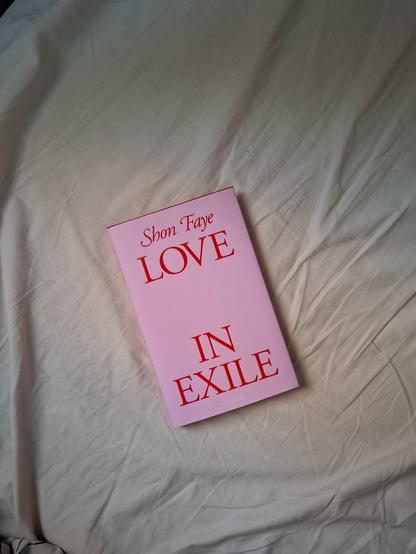Shon Fayen vaaleanpunainen kirja Love in Exile valkoisen lakanan päällä