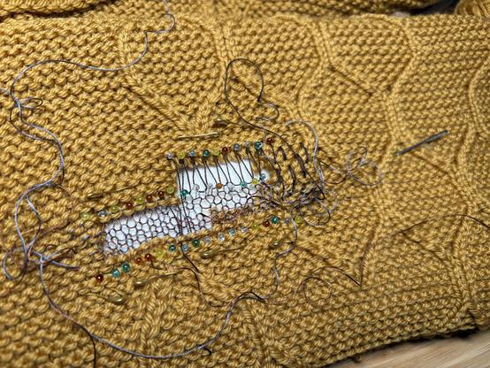 hole in a honey-coloured blanked featuring a pattern of hexagons, tidily prepared with pins and helper threads for swiss darning