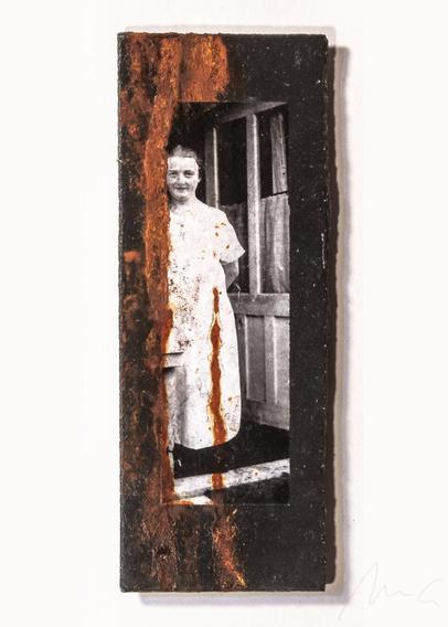 auf einer schwarzen eternitplatte ein S/W-foto einer mittelalten frau in einem weißen kittel mit zurückgebundenen haaren, einem offenen gesicht mit freundlich-sanftem lächeln, die in einer offenen balkontür oder tür zum garten steht. links neben und teils auch auf dem foto gibt es mehrere vertikale rostrote streifen, wie eine angetrocknete flüssigkeit.