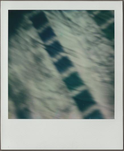 Polaroid of tea towel with blocks of dark blue running down the middle; it’s all blurry, in motion, kind of on a diagonal.
