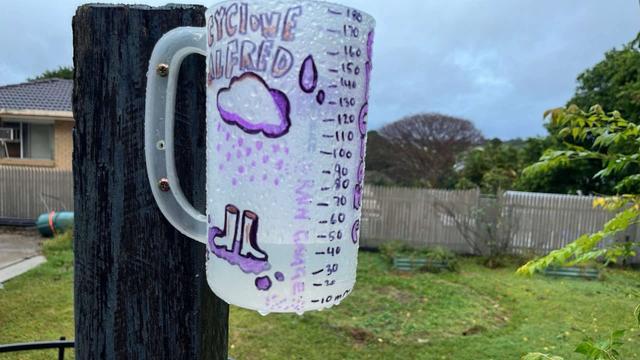 A home made rain gauge decorated with the words ‘cyclone Alfred’, a rain cloud, raindrops, and gumboots, reading approximately 45mm.