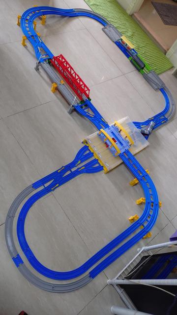 Blue plastic train track. There's a red bridge, a grey bridge and 3 stations, 1 elevated atop another.