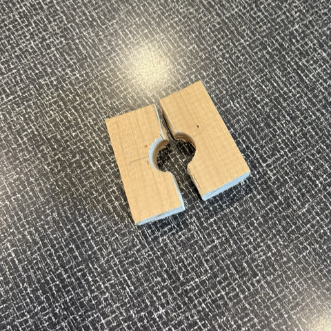 Two small pieces of wood which, when clamped together, form an approximate square with a hole of 22 millimeter diameter in the middle. The two pieces are split across the center of this hole.