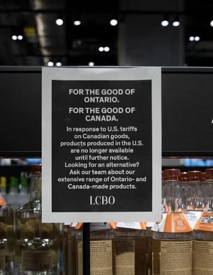 A sign is displayed in a store, with bottles of alcohol visible on the shelves below it. The sign reads:

"FOR THE GOOD OF ONTARIO. FOR THE GOOD OF CANADA. In response to U.S. tariffs on Canadian goods, products produced in the U.S. are no longer available until further notice. Looking for an alternative? Ask our team about our extensive range of Ontario- and Canada-made products. LCBO"