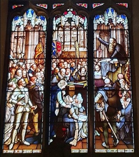 The bottom panel of the stained glass window. It depicts the Earl of Moray's funeral, with Reformationist Minister John Moore in a balcony (to the right), speaking to the crowd. The crowd is composed of a large number of well-dressed noble men (there are no women) packed tightly in the room. All are standing, except a scant few men in the front of the images, who are kneeling and weeping with grief.