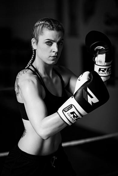 Portrait einer Kickboxerin, die im Ring steht und ihre mit Boxhandschuhen bekleidete Fäuste  angehoben hat