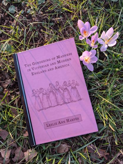 The book "The gendering of madness in Victorian and modern England and America" by Leslie Ann Harper lies in the grass next to a bunch of purple crocuses