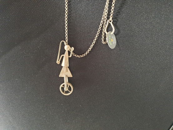 Collier en argent d'un personnage à queue de cheval sur un monocycle. 
Bijou fait à la main.