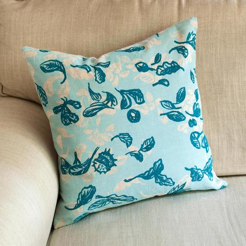 A hand printed cushion with conkers and leaves in blues.
