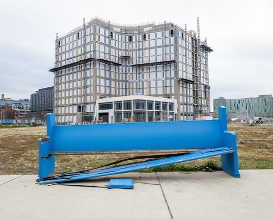 Broken blue wooden bench left on a sidewalk in front of an office building in the distance