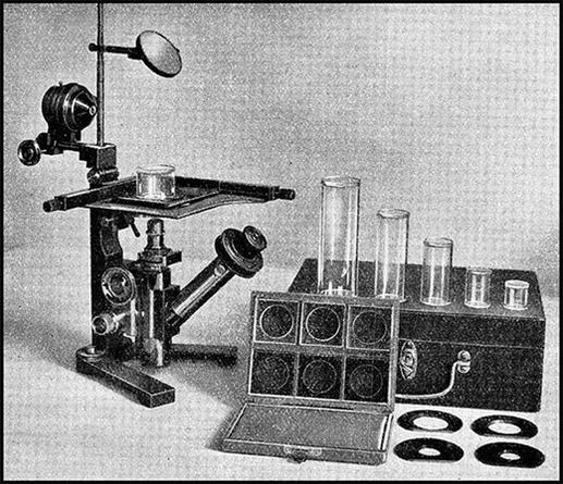 image/jpeg a historical photo of a microscope with a distinct bottom mounted lens system that points upward. A series a glass tubes with wooden a box of glass slide plates sits to the side. Image from Utermöhl (1931).