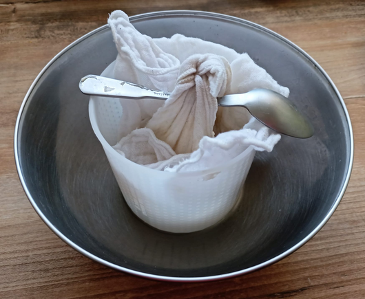 Der in ein Tuch eingeschlagene Joghurt hängt über einem Gefäß zum abtropfen
