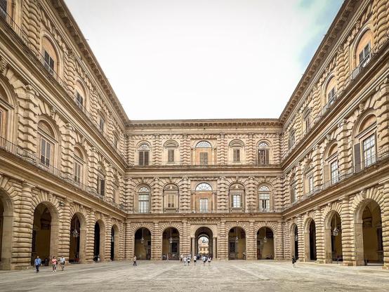 Corte interna di Palazzo Pitti a Firenze, con la sua imponente architettura rinascimentale. La corte è ampia e lastricata, con facciate in pietra che si sviluppano su più livelli, caratterizzate da archi e finestre. Si possono vedere persone che passeggiano nella corte, dando un senso di scala all'edificio. La luce del cielo illumina l'intera scena, mettendo in risalto i dettagli architettonici del palazzo.