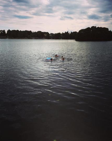 "In this photo, two individuals are enjoying a swim on a lake, under an overcast sky. The water appears calm, suggesting a peaceful and relaxing atmosphere."