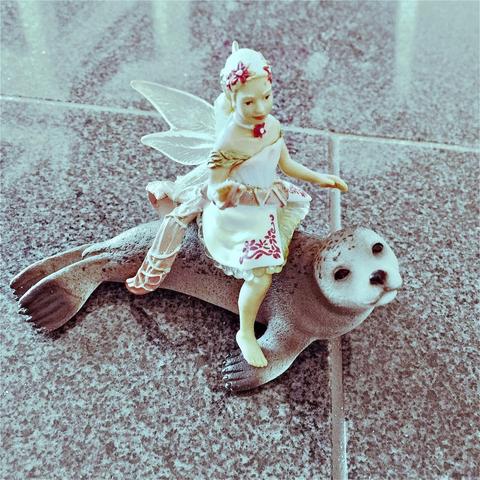 "An image of a toy scene featuring a figurine on a mermaid's back riding a seal or walrus. The mermaid is holding an anchor, suggesting an underwater theme. There's a playful and whimsical mood to the image."