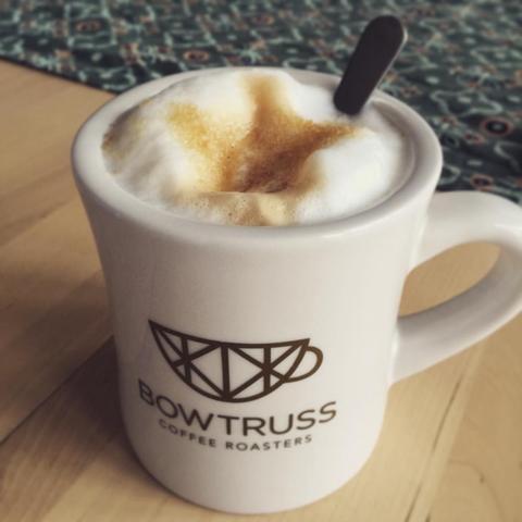 "A white mug with a latte art design, bearing the Bowtie Coffee logo, placed on a surface."