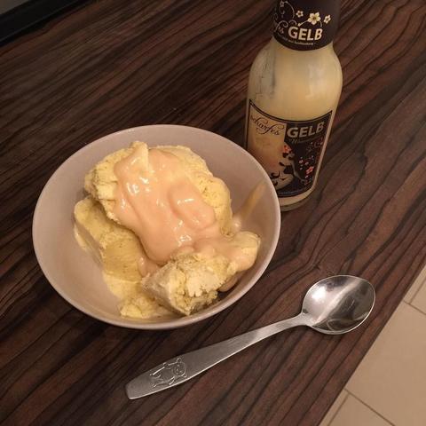 This picture shows a bowl of ice cream topped with caramel sauce on a dining table, next to a bottle of beer or a similar beverage. The mood seems to be casual and indulgent, suggesting a moment of leisure or relaxation, possibly after a meal or as a treat for oneself.