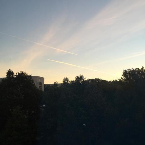 "This picture shows a serene scene at dusk, featuring a clear sky, white clouds, and a view of silhouetted trees and buildings, viewed from a window. The mood is tranquil and peaceful."