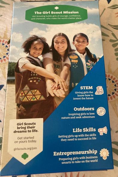 The back of a box with a picture of 3 girls. 
Text: 
The Girl Scout Mission:
Girl Scouting builds girls of courage, confidence, and character, who make the world a better place. 

STEM Giving girls the know-how to invent the future 

Outdoors Inspiring girls to love nature and seek adventure 

Girl Scouts bring their dreams to life. Get started on yours today. girlscouts.org/join 

Life Skills 
Setting girls up with the skills they need to succeed in life 

Entrepreneurship 
Preparing girls with business smarts to take on the world