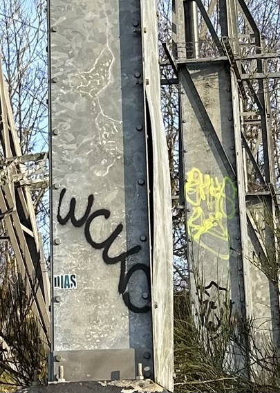 A photo showing a close up view of an electricity pylon connector. The protective shielding on the connector has been pried open a fraction. There is black and yellow graffiti on the pylon.