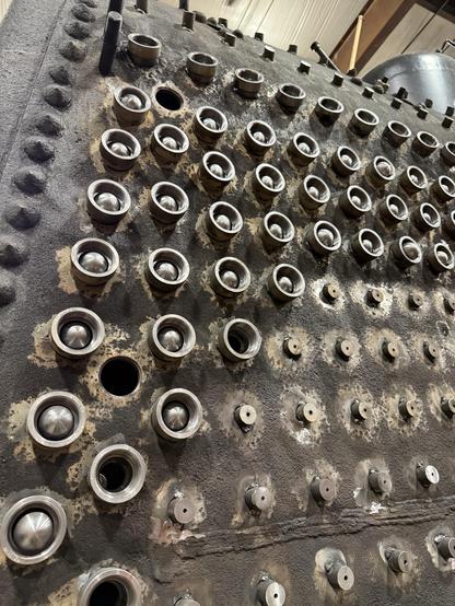 The outside of a locomotive firebox, with rigid stays tacked in and many collars for flexible stays installed, many with the ball ends of flexible stays installed