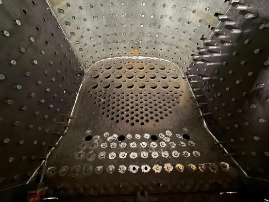 The inside of a locomotive firebox, with many holes for boiler tubes in the sheet ahead, and stay bolts sticking through holes on all sides