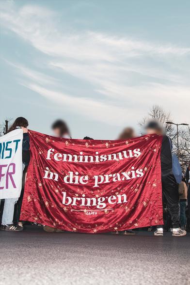 Transparent mit dem Text "Feminismus in die praxis bringen" von unten mit Blitz fotografiert.