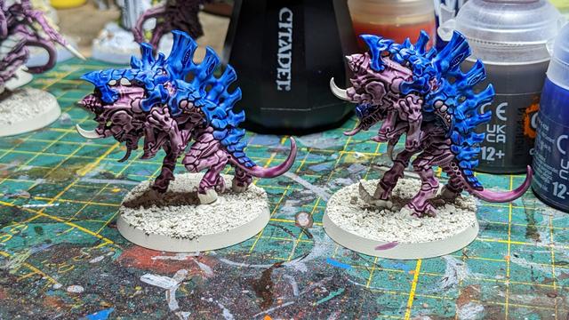 Two Tyranid models painted in purple and blue on white bases.