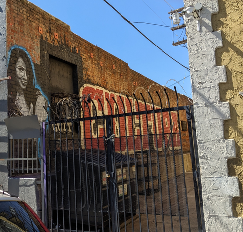 mural of a woman's face and Cultura behind a spiked gate in an alley