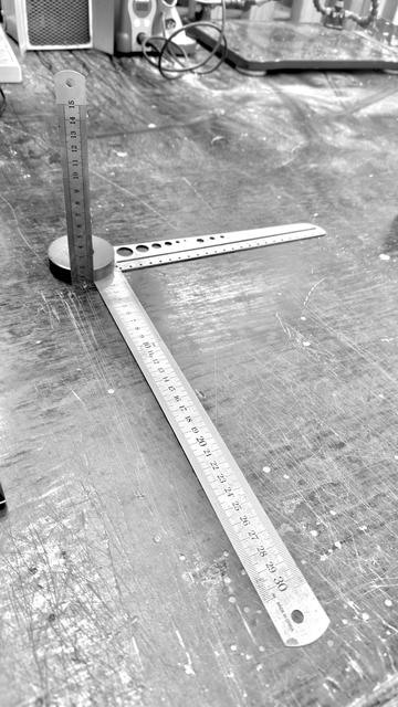 One rule to measure them all... well, in 3 dimensions. One for each. Three metal rules of different sizes and kinds are arranged such that all zero points on each axis meet at a conveniently placed magnet, which holds them together and holds the x-axis (depth/height) upright. Grayscale.