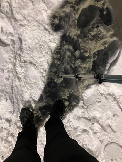 Perspective of the runner looking down at her spike clad shoes and nordic poles on a snow covered path.