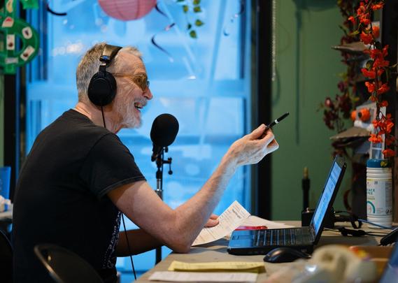 A man wearing headphones gesticulates with a writing implement.