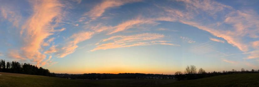 ein breites Panorama von blauem Himmel mit bunten Wolken in einem Bogen. orange Farbe am Horizont