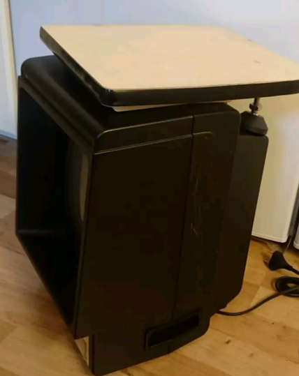 A Vectrex games console with a piece of wood on top, functioning as a shelf space one can use for various lightweight things.