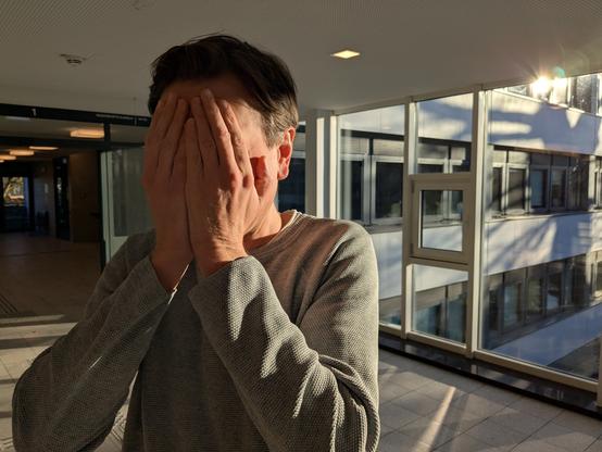 Thilo steht vor dem Saaltrakt des Lübecker Gerichtshauses. Er versteckt sein Gesicht verschämt hinter seinen Händen.