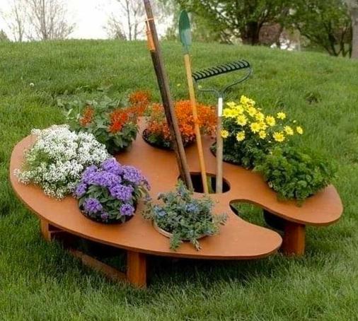 Foto van grote tafel in de vorm van een schilderspalet. In plaats van verf zijn er kleurige planten in gezet. In plaats van kwasten tuingereedschap.
