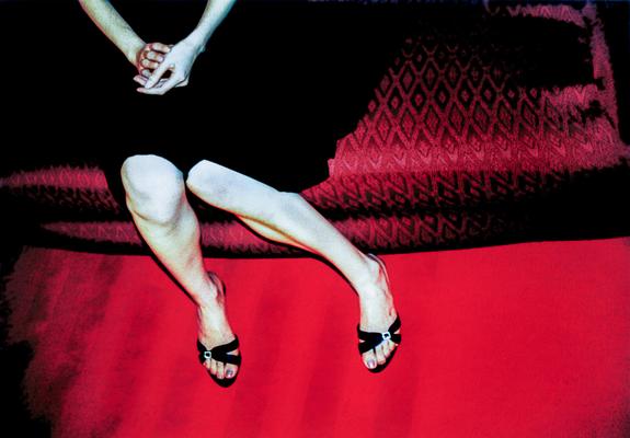 The lower part of a lady, posing for me sitting dressed in black, pale skin, on a red brocade sofa over an intense red carpet. A moody, romantic, nostalgic shot.