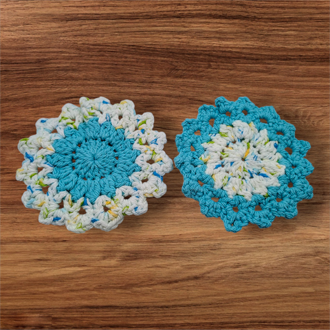 Two crocheted coasters in turquoise and a white, yellow, green, and blue multicolor yarn. The pattern looks floral and one coaster is multi in the center and turquoise on the outside while the other one is the opposite.