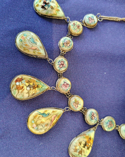 Necklace with small floral circular pieces from which are suspended larger teardrop pieces with individual motifs
