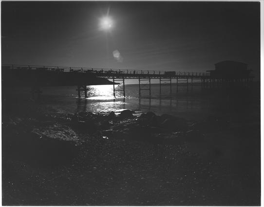 Photo of totland pier, Isle of Wight with the beach in foreground as the sun sets behind.