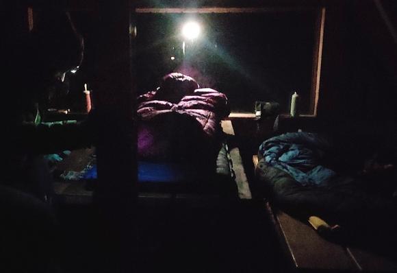 Schutzhütte am Rennsteig. Mit Isomatten und Schlafsäcken auf dem Tisch und den beiden Bänken links und rechts 
 I'm Hintergrund hängt eine Lampe